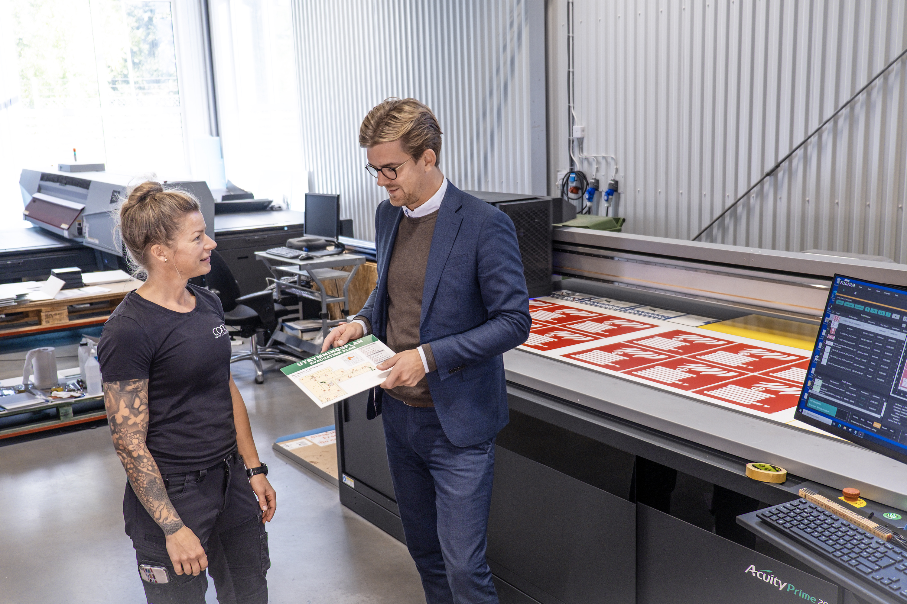 Bild på vd:n Johan Calmestrand som diskuterar skärpan i en planprintad utrymningsplan med skyltmakaren Sara Arvén. 